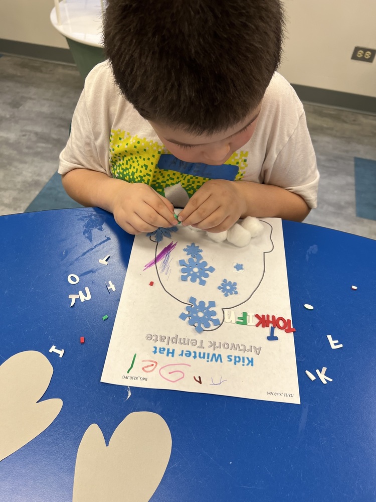 student gluing cotton balls and snowflakes on a paper hat