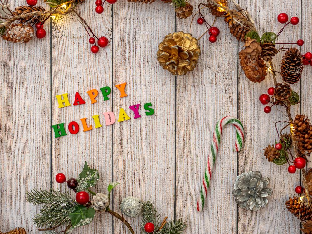 happy holidays written on wood background with holiday garland and candy canes around it