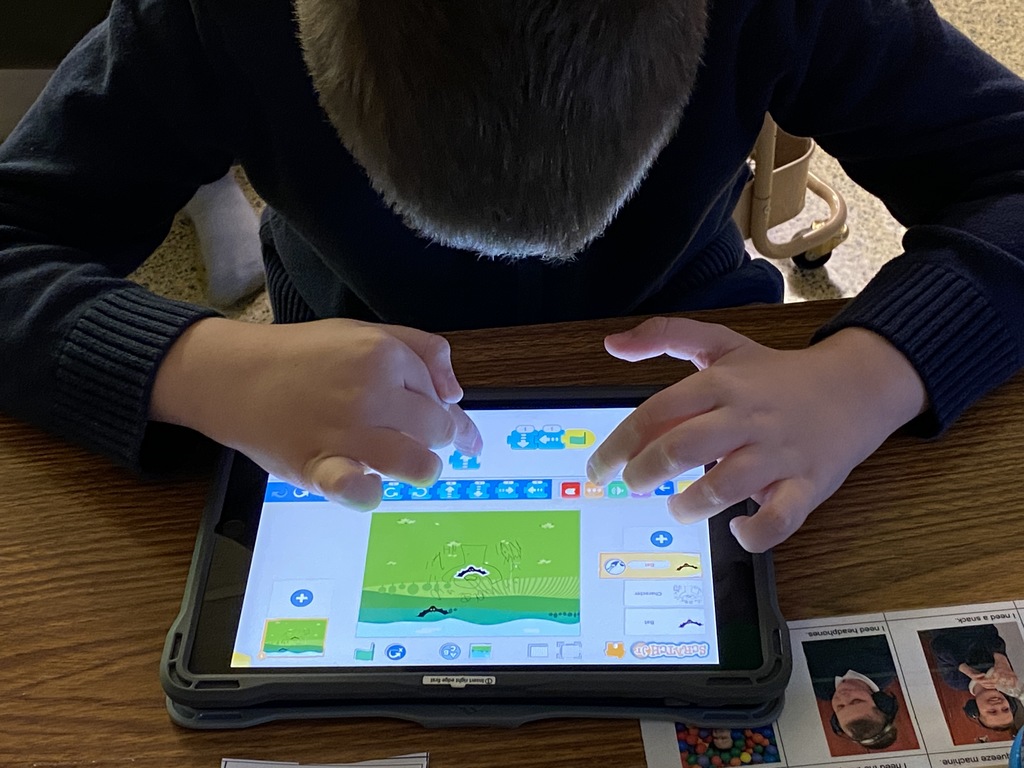 male student looking down and touching icons on Scratch Jr app on iPad