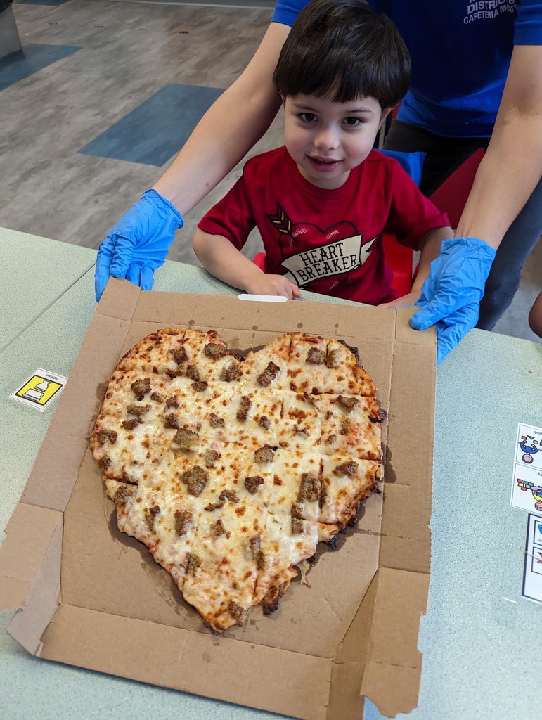 student standing behind a heart shaped pizza